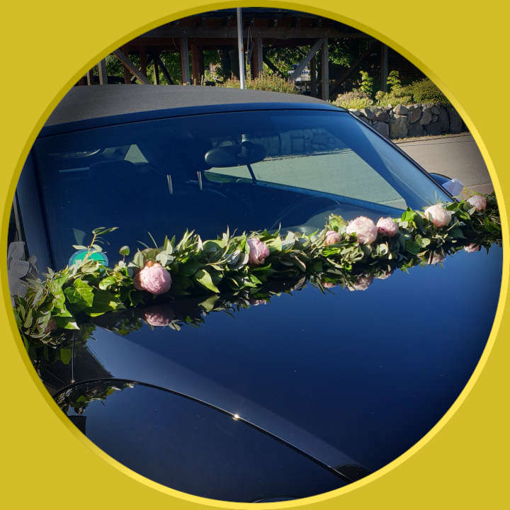 Autoschmuck in Form einer Blumengirlande vor der Windschutzscheibe des Hochzeitsautos.