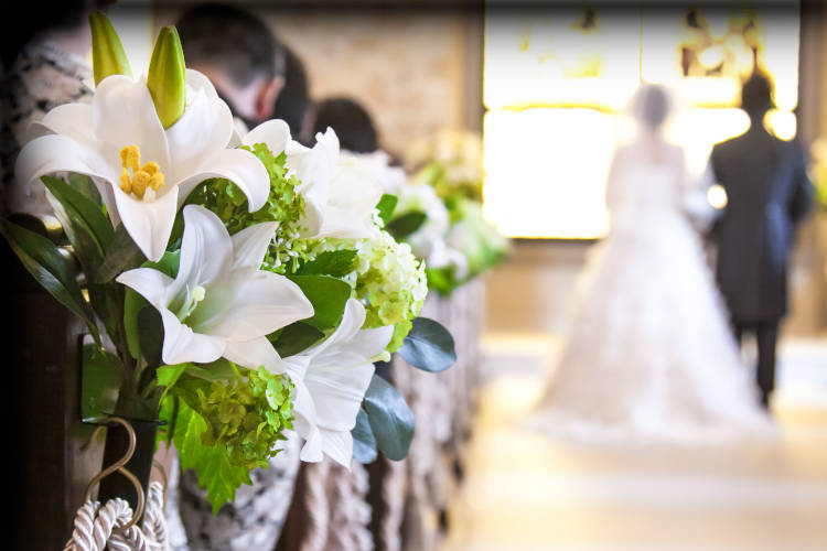 Hochzeitspaar in einer Kirche. An den Bänken der Gäste wurden dekorative Blumengebinde befestigt.
