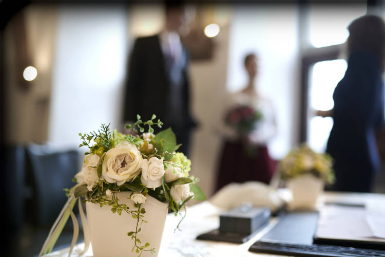 Braut und Bräutigam sowie der Standesbeamte befinden sich im Hintergrund. Im Vordergrund eine dekorative Vase mit schönen Blumen zur Hochzeit.