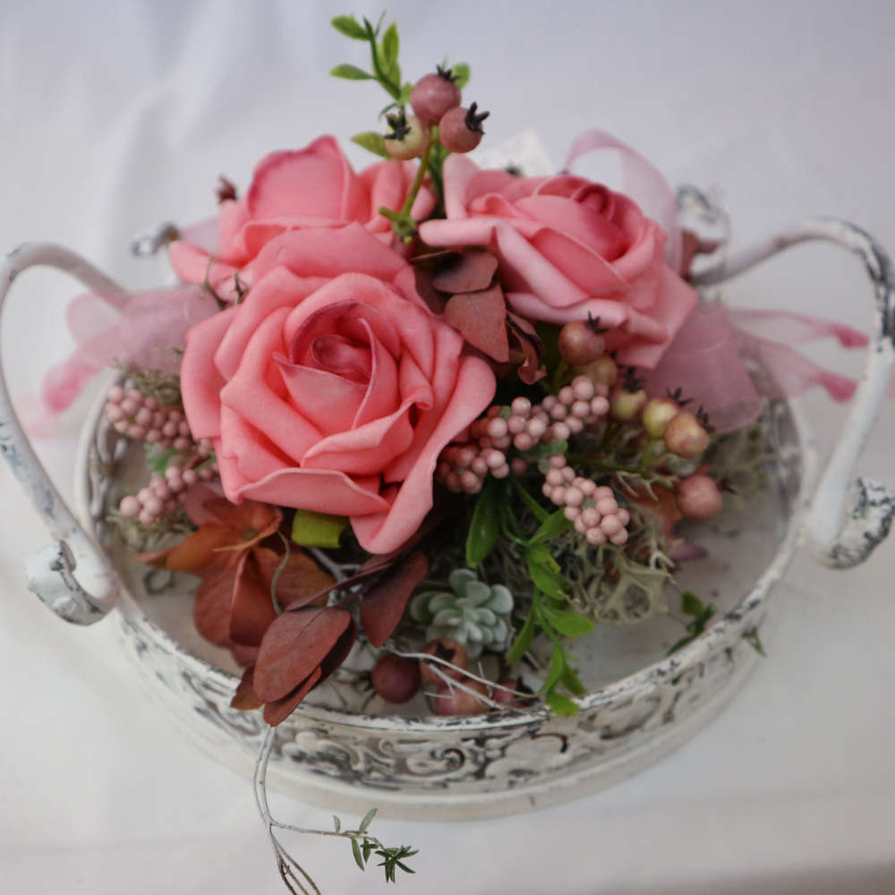 Ein Dekotablett im Vintage-Stil, welches mit Kunstblumen und Kunstbeeren in rosa dekoriert wurde.