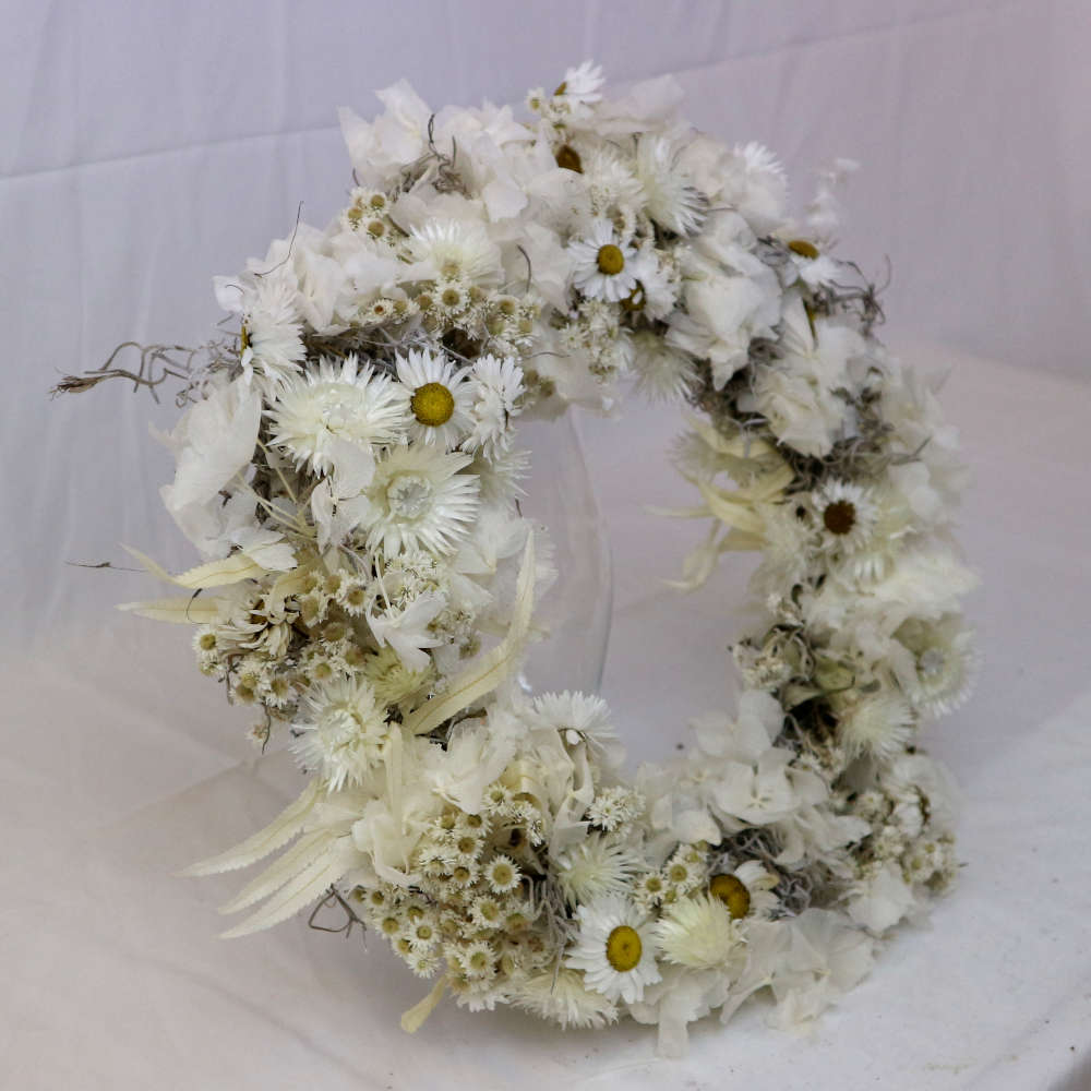 Ein weißer Kranz aus getrockneten Blumen. Unter anderem wurden Strohblumen und Hortensieblüten verwendet. Streng gewickelte Variante.