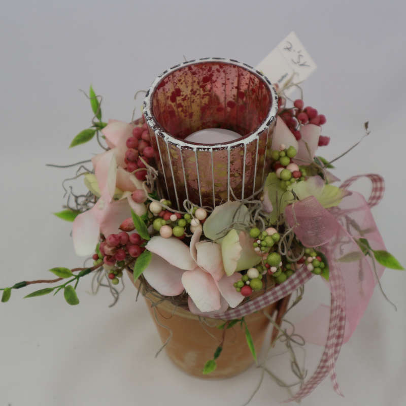 Kerzenglas im kleinen Tontopf, umgeben von Kunsthortensienblüten, Kunstbeeren und getrockneten Pfefferzweigen.