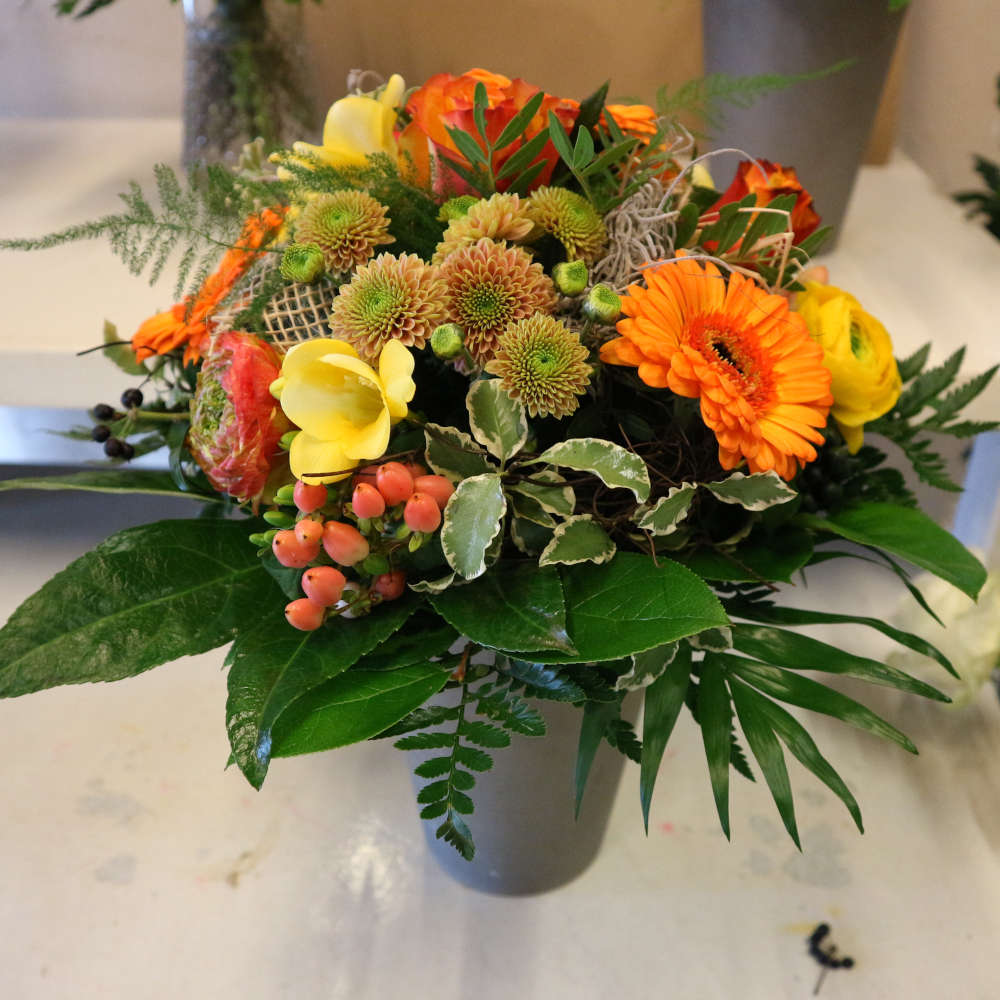  Ein großer, kompakt gebundener Blumenstrauß, bestehend aus orangen Gerbera und orange-gelben Rosenblüten; ergänzt um gelbe Blüten. 
