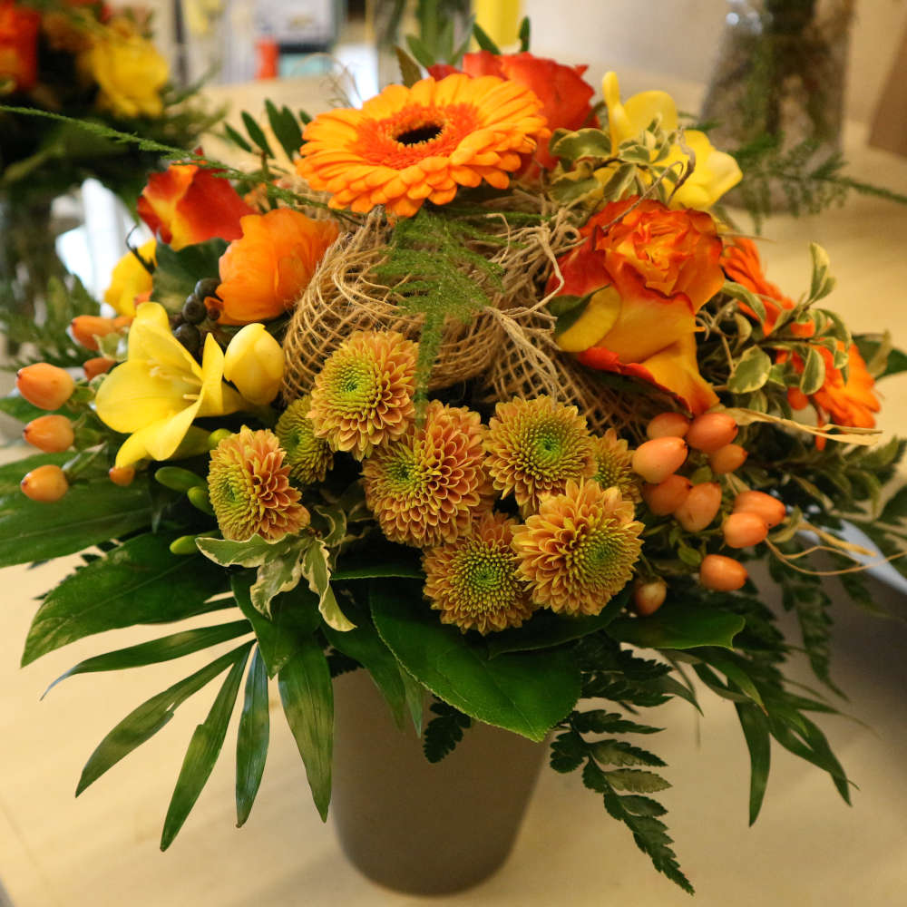 Ein großer, kompakt gebundener Blumenstrauß, bestehend aus orangen Gerbera und orange-gelben Rosenblüten; ergänzt um gelbe Blüten.