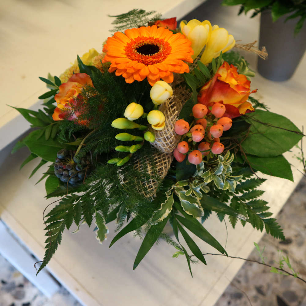  Ein kleiner, kompakt gebundener Blumenstrauß, bestehend aus orangen Gerbera und orange-gelben Rosenblüten; ergänzt um gelbe Blüten. 