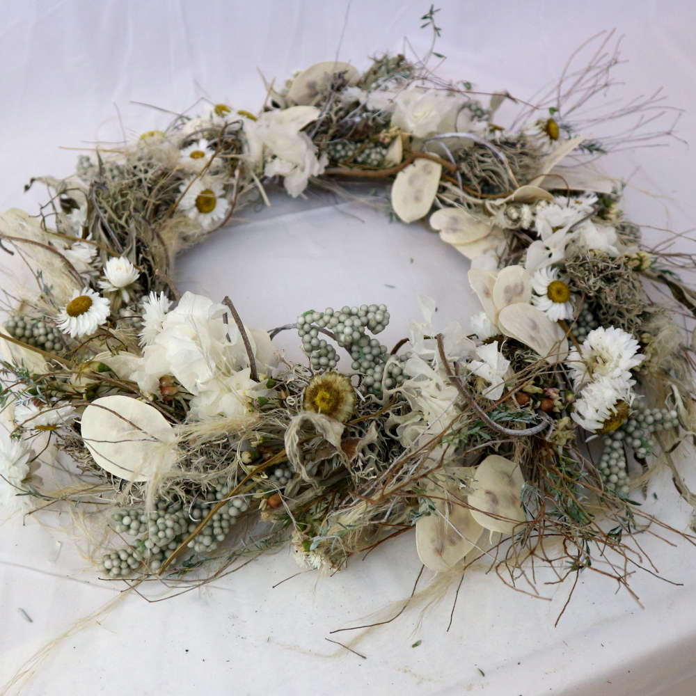 Ein weißer Kranz aus getrockneten Blumen. Unter anderem wurden Strohblumen und Hortensieblüten verwendet. Locker gewickelte Variante.