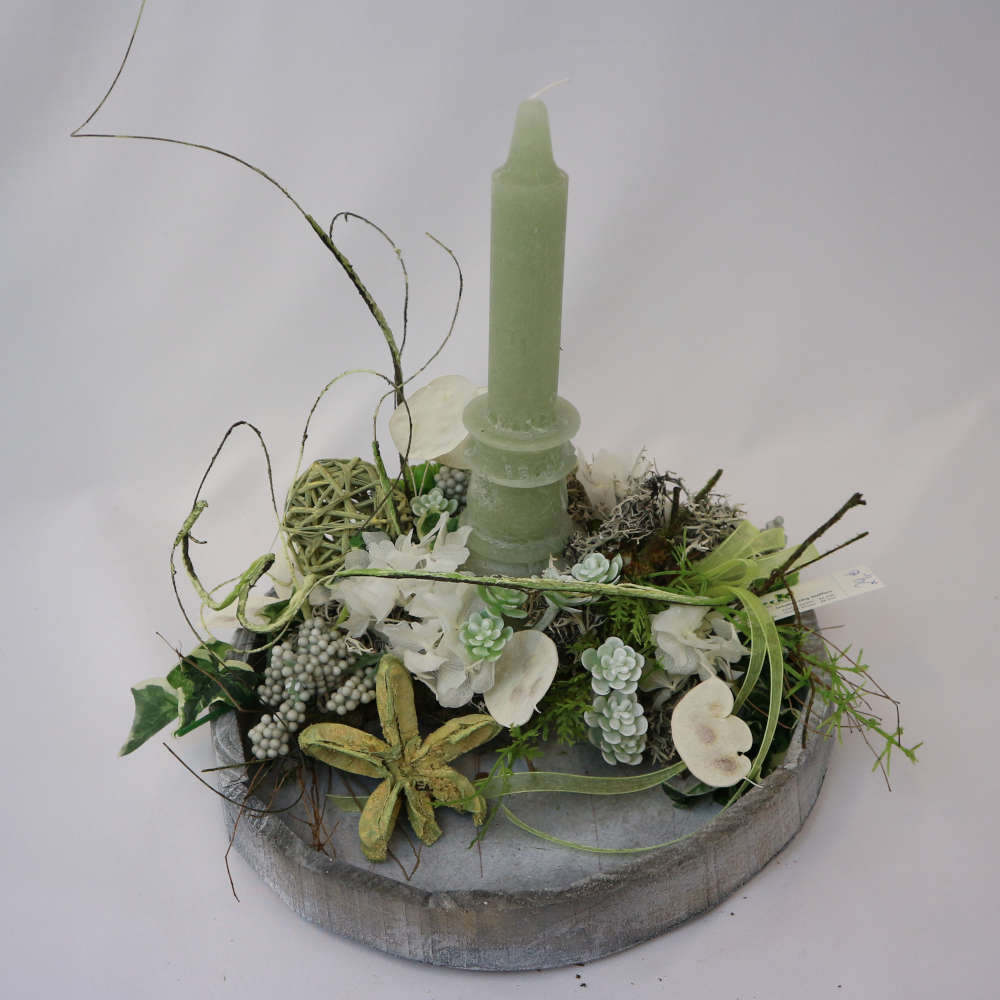  Ein Tablett in Holzoptik mit einer mintgrünen Kerze; grünen Kunstbeeren und getrockneten Blütenblättern. 
