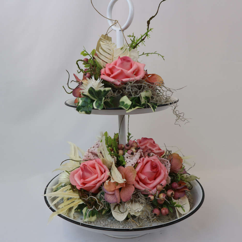 Eine zweigeschossige Etagere, welche u.a. mit rosa Kunstrosen und Kunstbeeren sowie getrockneten Strohblumen geschmückt wurde.