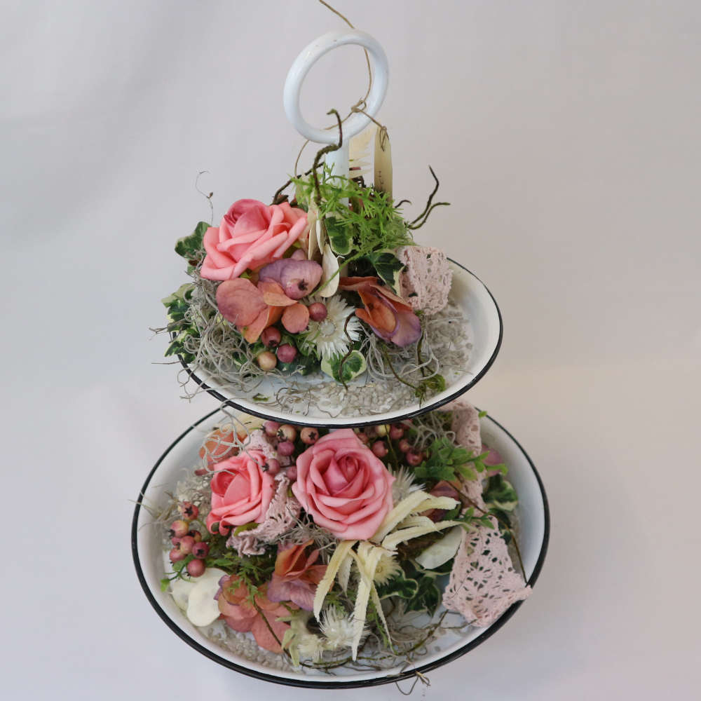 Eine zweigeschossige Etagere, welche u.a. mit rosa Kunstrosen und Kunstbeeren sowie getrockneten Strohblumen geschmückt wurde.