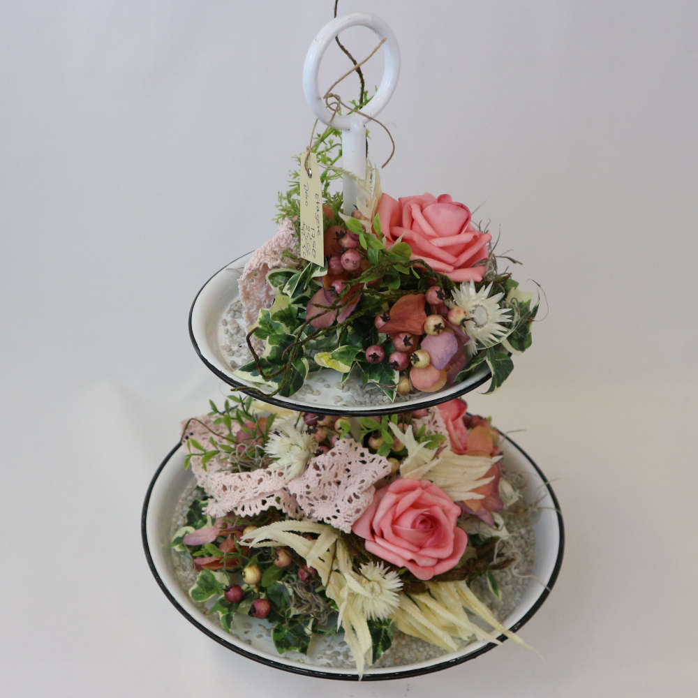 Eine zweigeschossige Etagere, welche u.a. mit rosa Kunstrosen und Kunstbeeren sowie getrockneten Strohblumen geschmückt wurde.
